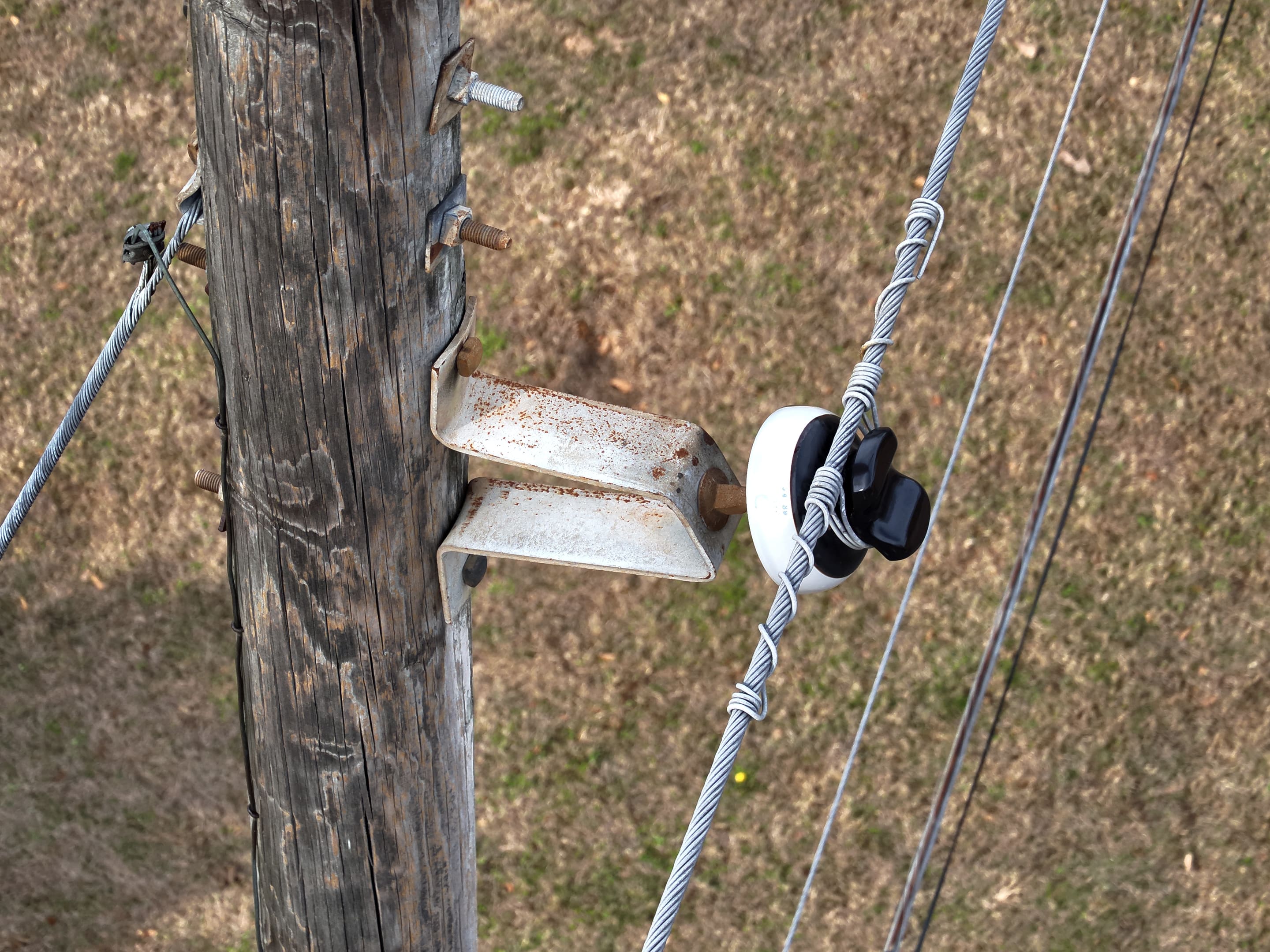 Drone close-up of a pole crossarm bracket and insulator with tie wire.